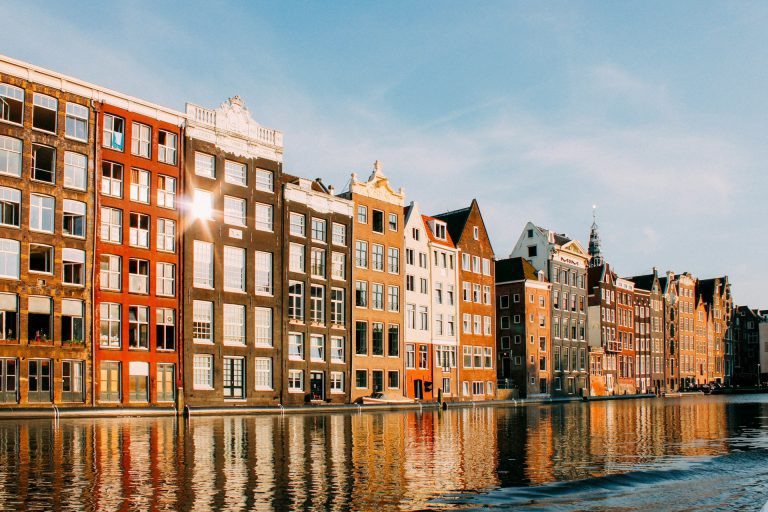 Amsterdã. Foto de edifícios de cores diversas ao lado de um corpo de agua.