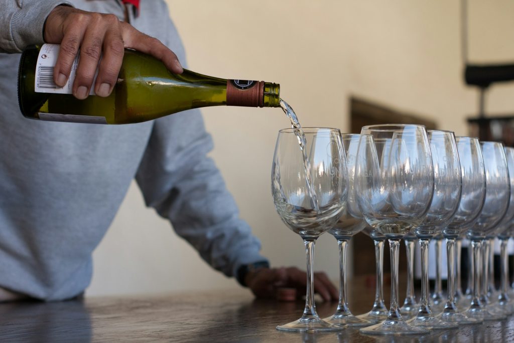 Foto de pessoa servindo vinho branco em taças transparentes.