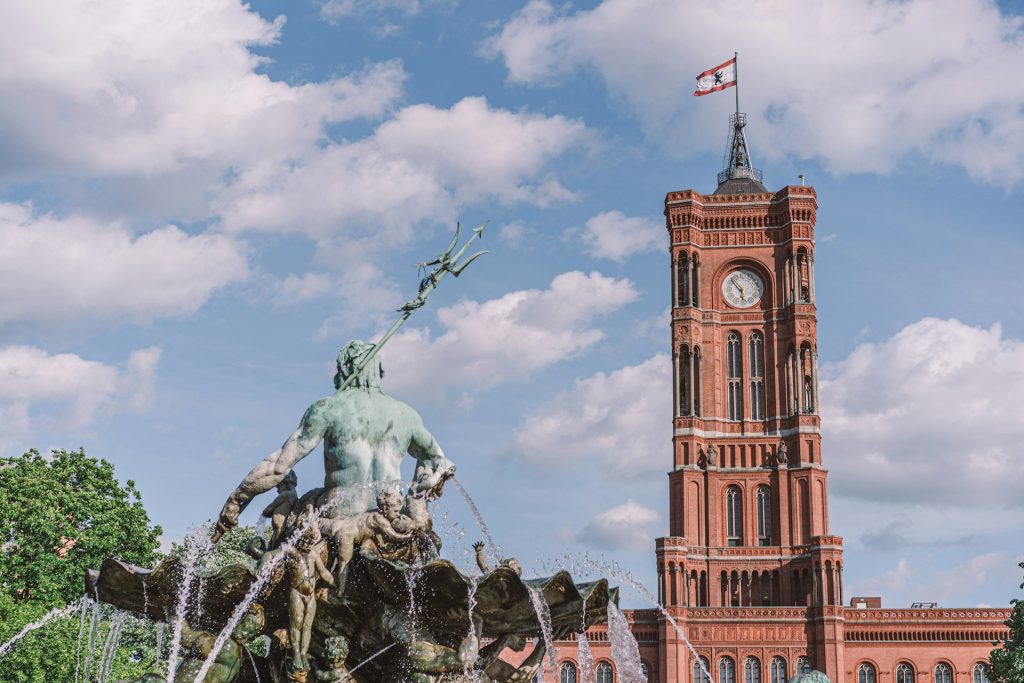 Neptunbrunnen. Escultura de concreto vista de trás, com edifício marrom ao fundo.