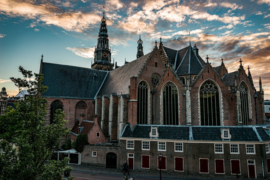 Oude Kerk. Grande edifício marrom com torre com um relógio ao fundo. 