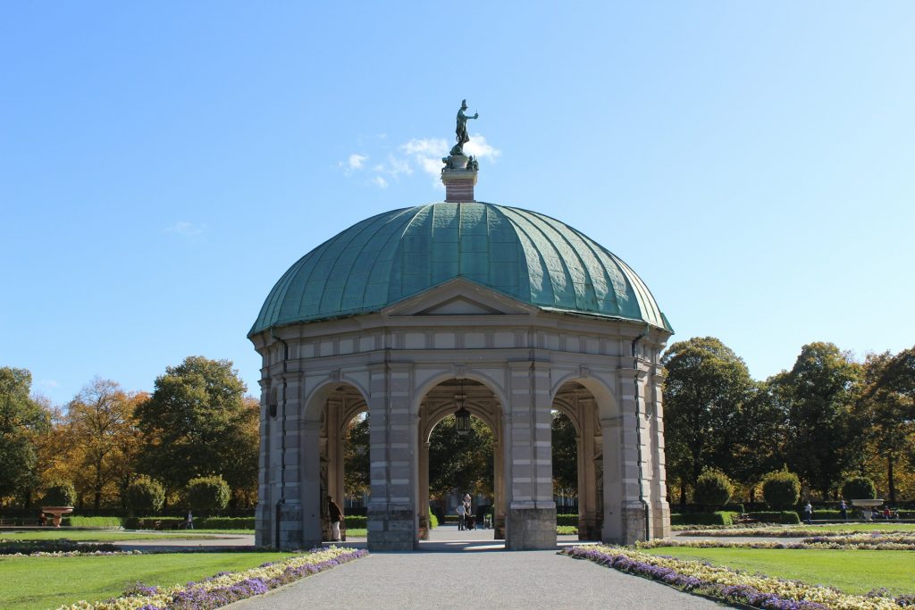 Templo de Diana. Edifício com colunas e cúpula verde no meio de um jardim. 