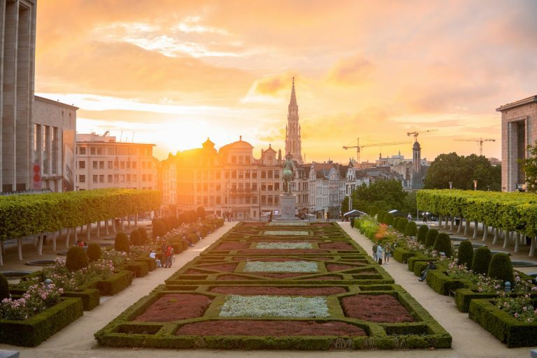 Bruxelas. Foto paisagem de um jardim com formas geometricas de flores coloridas com uma estatua e edificios ao fundo