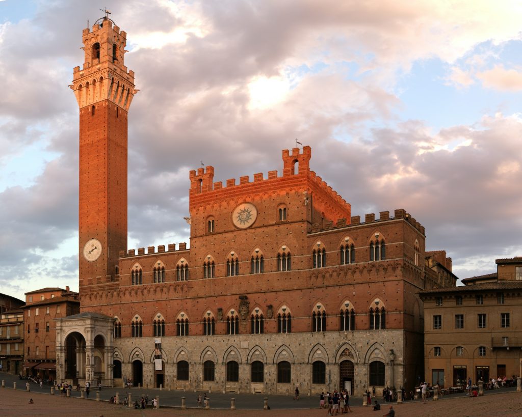 Siena. Foto de de edificio de concreto marrom com várias janelas e arcos.