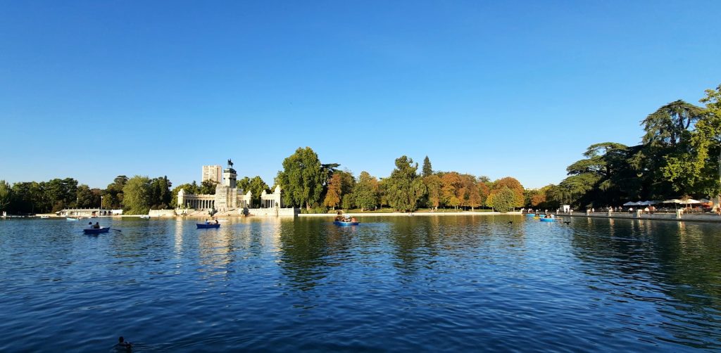 retiro madrid. corpo de agua e uma construção com varias torres ao fundo