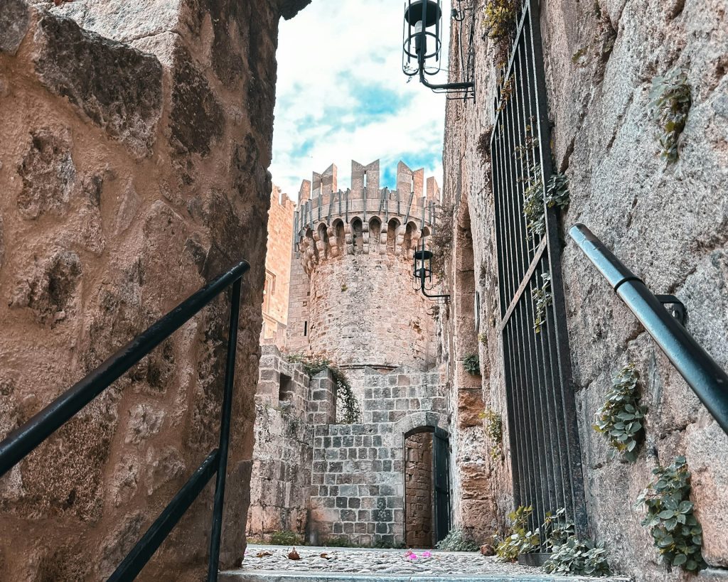 Foto de rua e construções antigas de pedra com grande portão de ferro.