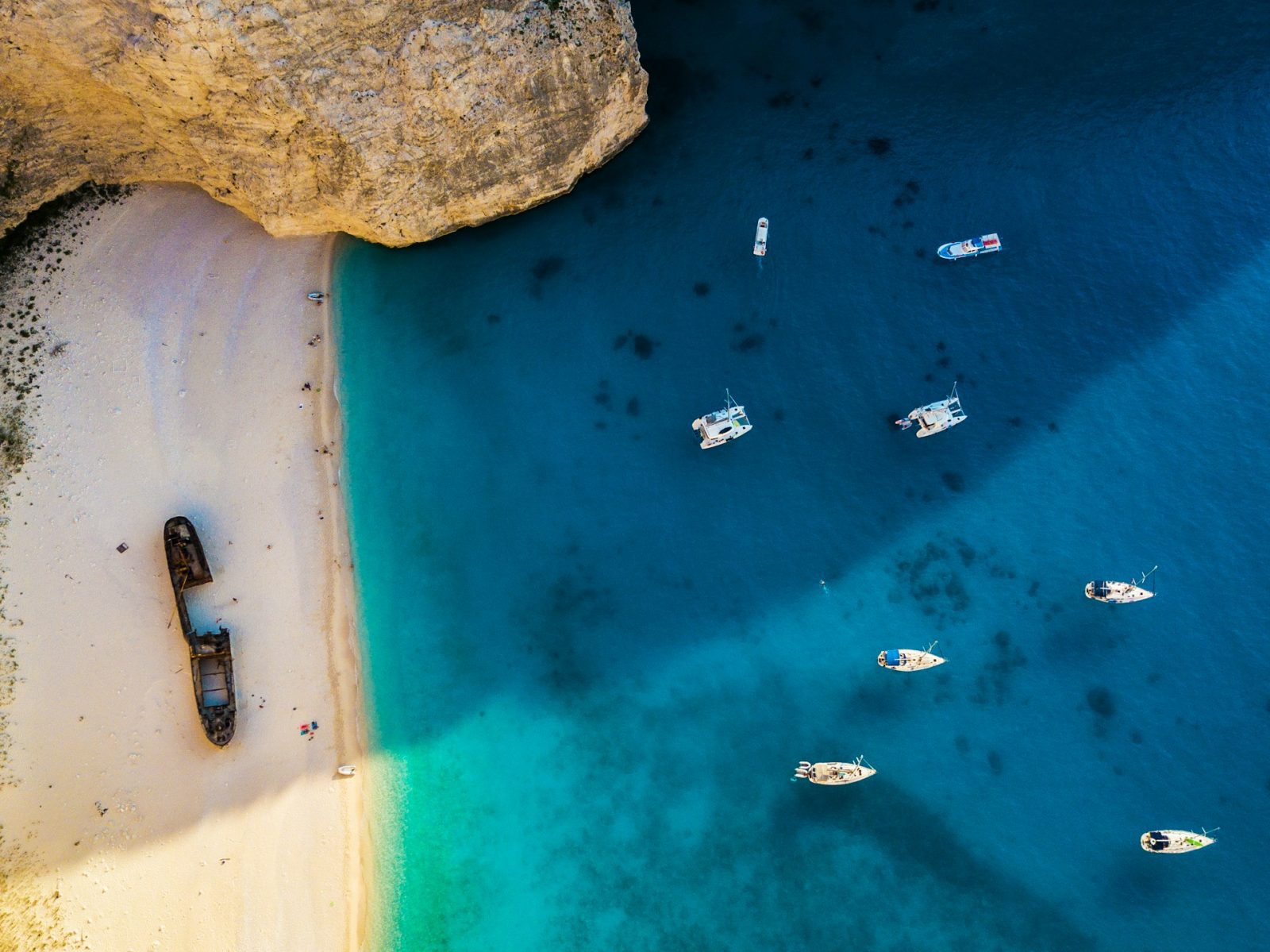 Grecia. Foto tirada de cima de uma praia cercada por montanhas e um navio naufragado na areia.