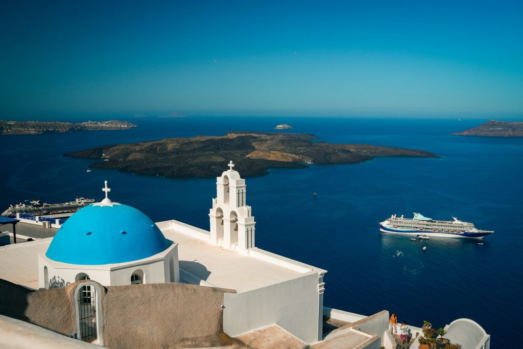 Santorini. Igreja branca com cúpula azul em frente ao mar azul.