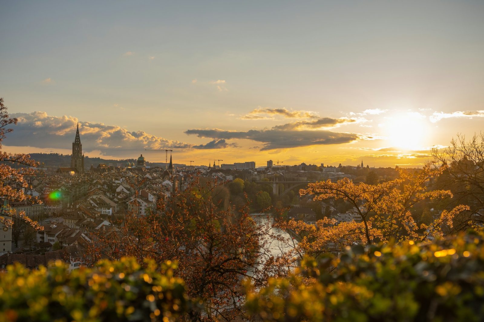 Berna. Foto de paisagem com vegetação alaranjada e cidade no final do dia.