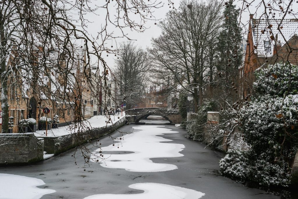 bruges. rio congelado que atravessa cidade coberta de neve.