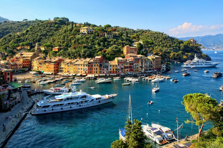 Foto de Portofino, Itália. Vista com iate branco e casas coloridas ao fundo.